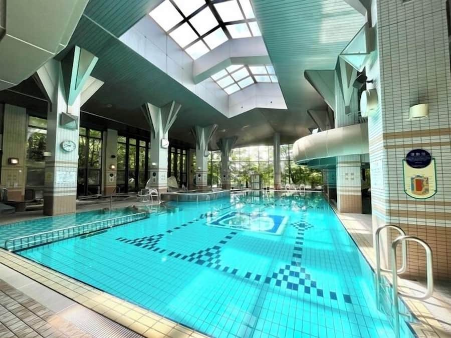 An indoor swimming pool with clear blue tiles, a skylight ceiling, and a tiled wall with a plaque.