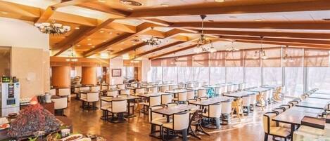 A spacious dining area with multiple tables and chairs, a central buffet with various dishes, and a modern ceiling design with recessed lighting.