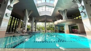 An indoor swimming pool with a high ceiling and skylights, surrounded by large pillars and a tiled floor. - Hotel Blancvert Nasu (Nasu)