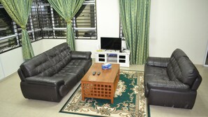 A living room with two leather sofas, a wooden coffee table, a TV on a white stand, and a patterned rug. - Sitiyam Homestay Kota Warisan (Sepang)