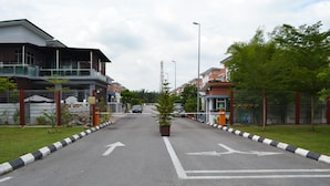 A street with two-way traffic, a central median with a plant, and buildings on either side. - Sitiyam Homestay Kota Warisan (Sepang)