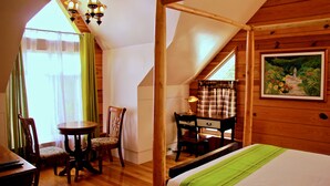 Un dormitorio con techo de madera, una cama con colcha verde, un escritorio con lámpara, una silla y una ventana con cortinas.