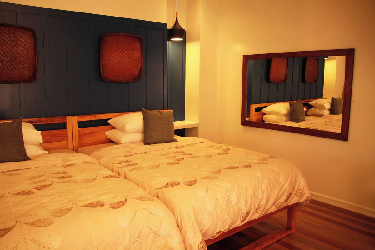 Een tweepersoonsbed met een houten hoofdbord, een nachtkastje en een spiegel aan de muur.