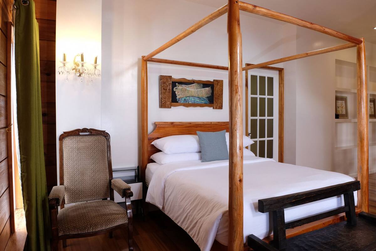 Een bed met baldakijn en houten hoofdeinde, een stoel en een nachtkastje.