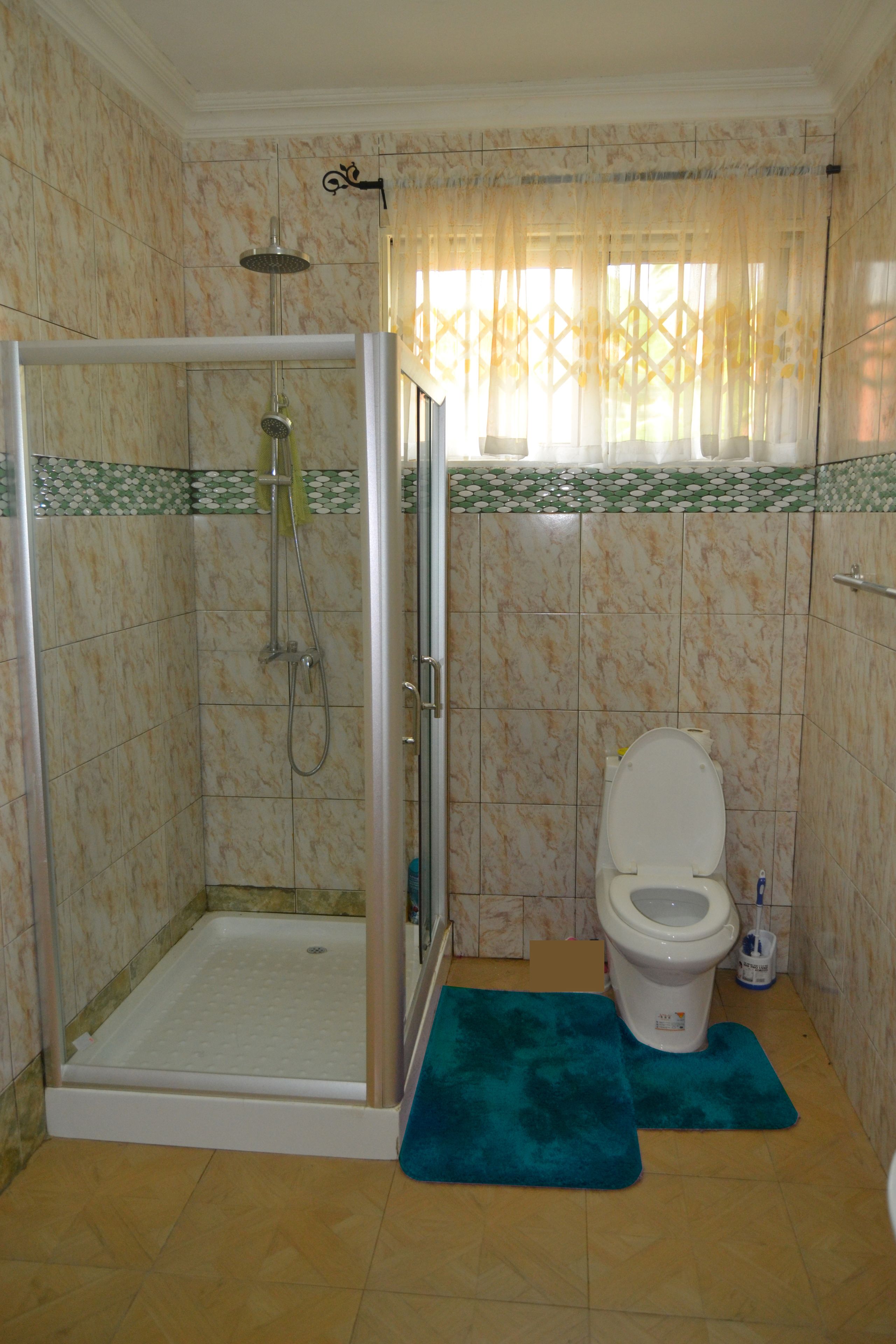 A bathroom with a shower enclosure, toilet, and a window with patterned curtains.