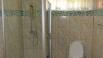 A bathroom with a shower enclosure, toilet, and a window with patterned curtains.