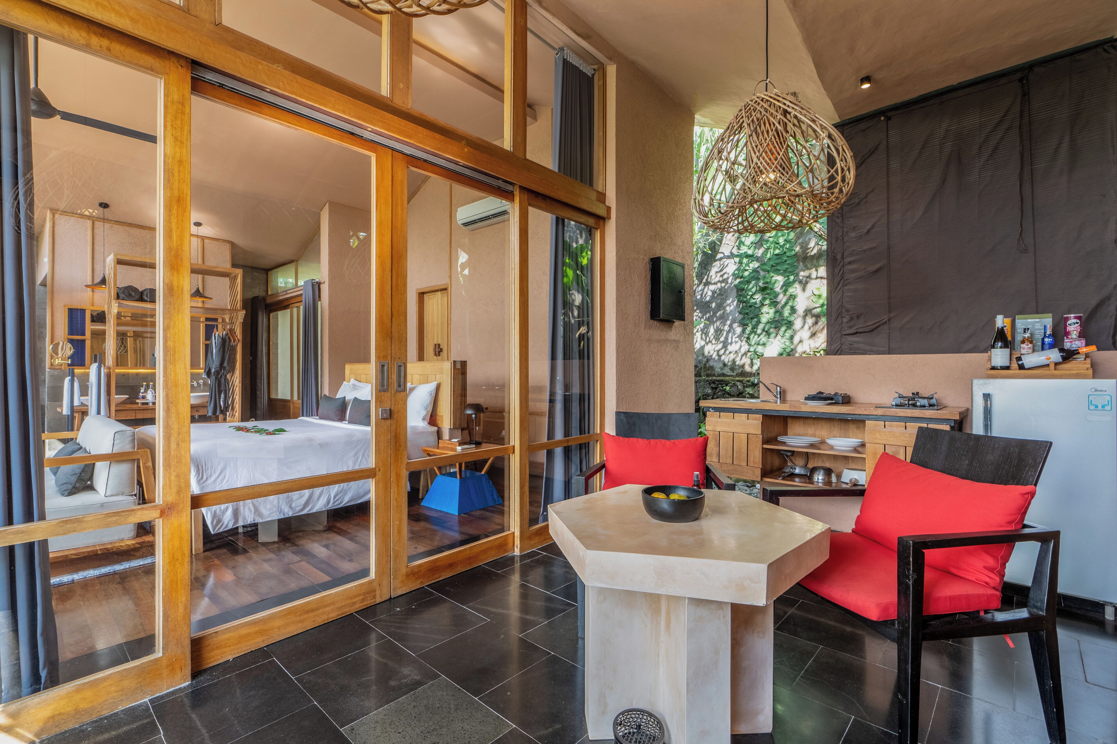 A modern hotel room with a large bed, a dining area with a table and chairs, and a kitchen area.