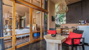 A modern hotel room with a large bed, a dining area with a table and chairs, and a kitchen area.