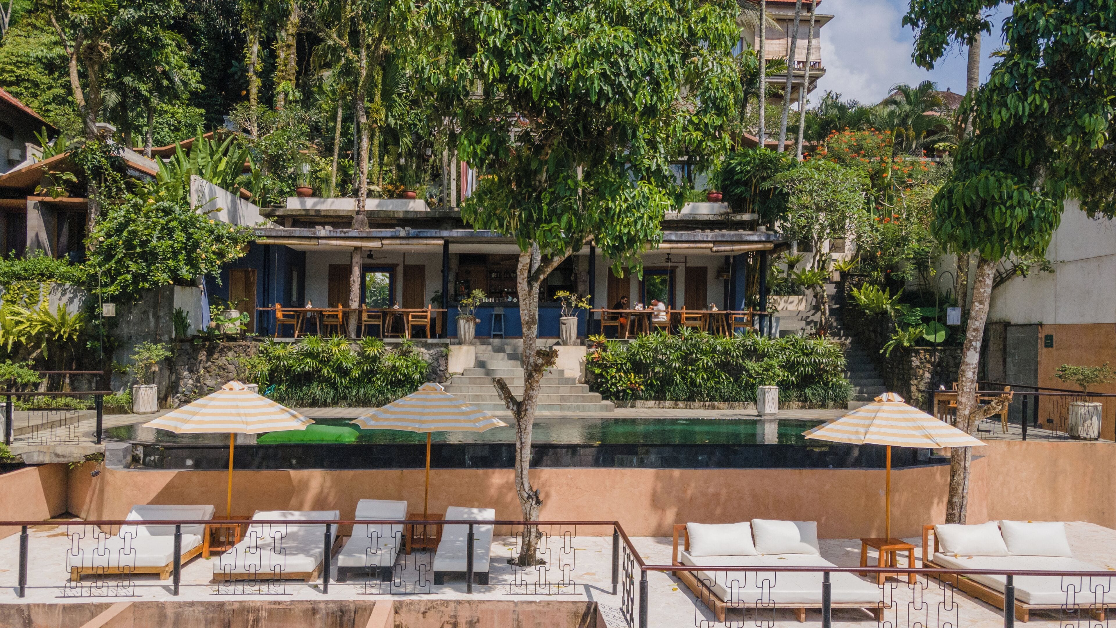 Un hotel con zona de piscina, sillones de descanso y mobiliario exterior.