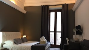 Habitación de hotel con dos camas, un sofá, un escritorio con lámpara y vistas a un balcón nevado.