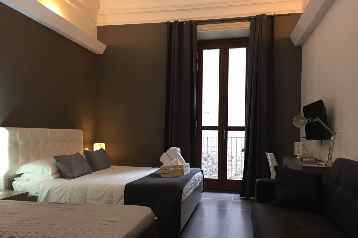 A hotel room with two beds, a sofa, a desk with a lamp, and a view of a snowy balcony.