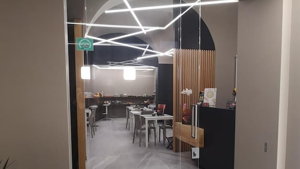 Un restaurante moderno con una zona de comedor central, una barra con menú y una escalera que lleva a un nivel superior.
