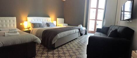 A hotel room with a large bed, two bedside tables with lamps, a sofa, and a TV mounted on the wall.