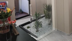 Zona de recepción con un separador de vidrio, un pequeño jardín interior y un mostrador de recepción con un jarrón de flores.