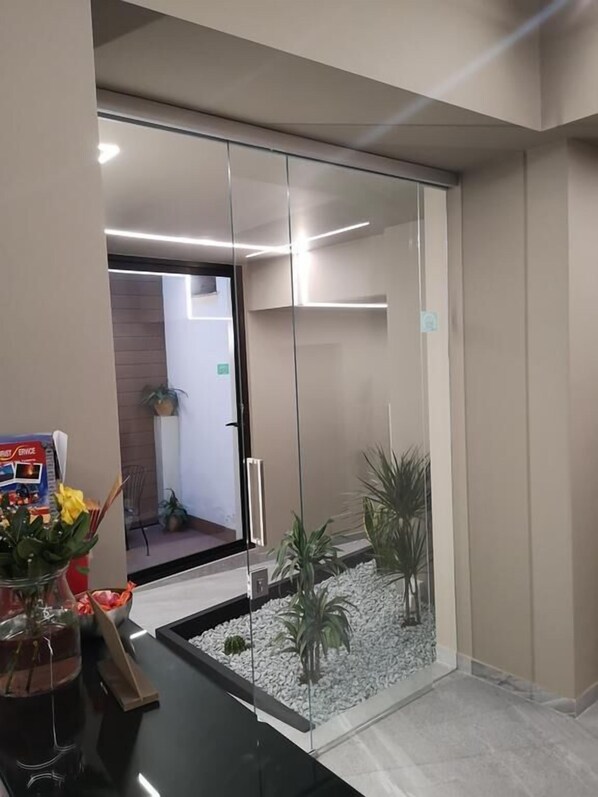 Un espace d’accueil doté d’une cloison en verre, d’un petit jardin intérieur et d’un comptoir de réception agrémenté d’un vase de fleurs.