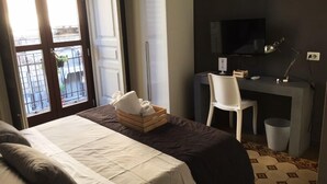 Habitación de hotel con cama, escritorio con silla, televisión y ventana con vista al exterior.