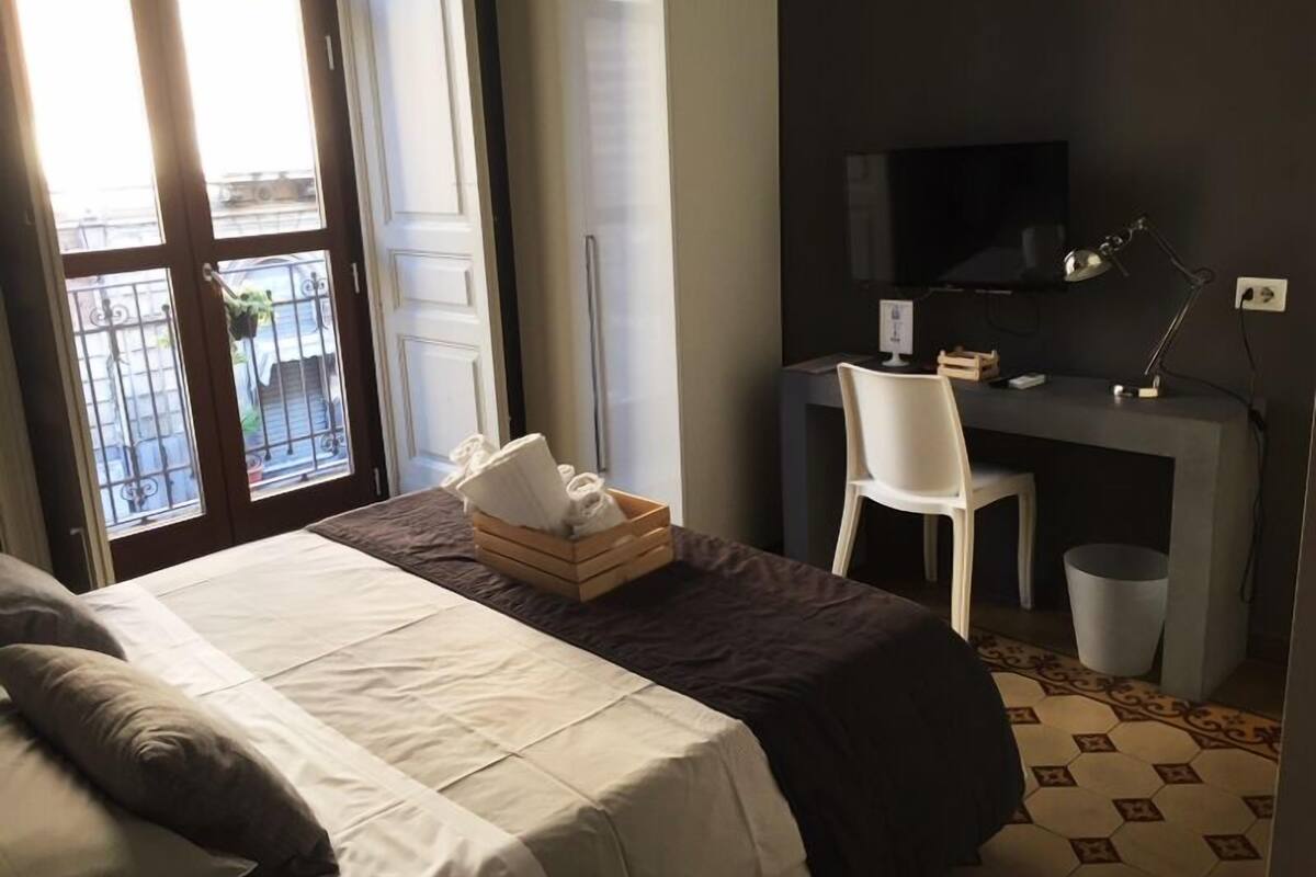 A hotel room with a bed, a desk with a chair, a TV, and a window with a view of the outside.
