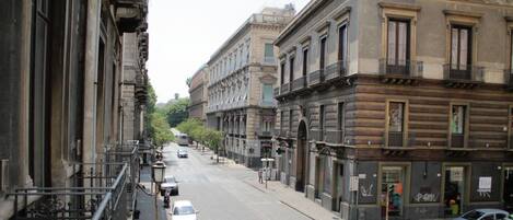 A street view with historic buildings, parked cars, and a clear sky.