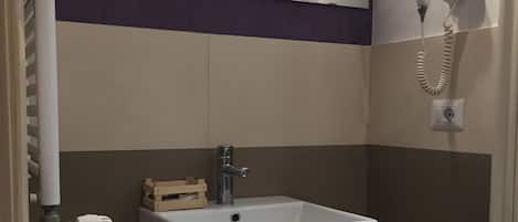 Un baño con lavamanos blanco, espejo, secador de pelo y toallero.
