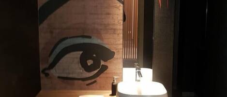 Un baño con un gran mural en la pared de un ojo, un lavamanos moderno y un espejo.