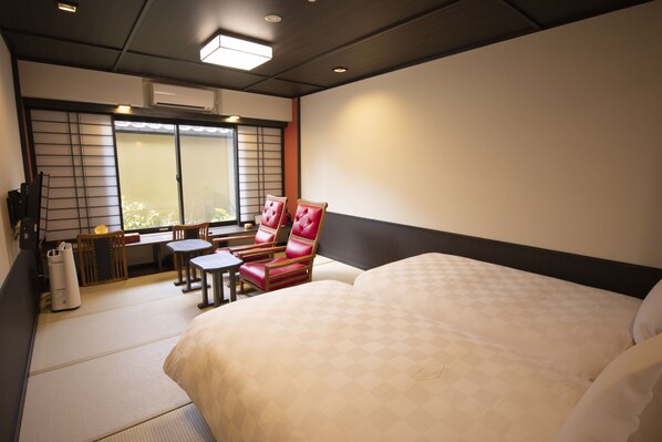 Habitación de hotel con una cama grande, un área de descanso con una mesa y sillas, y un balcón accesible mediante una puerta corredera.