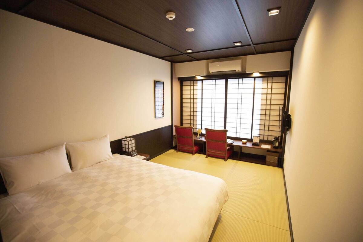 Ett hotellrum med en stor säng, ett skrivbord med stolar och utsikt genom en shoji-skärm.