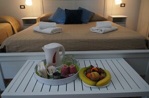 A neatly made bed with towels, a bedside table with a kettle and glasses, and a breakfast tray with fruits and a cup. - Casa Laganà (Reggio Calabria)