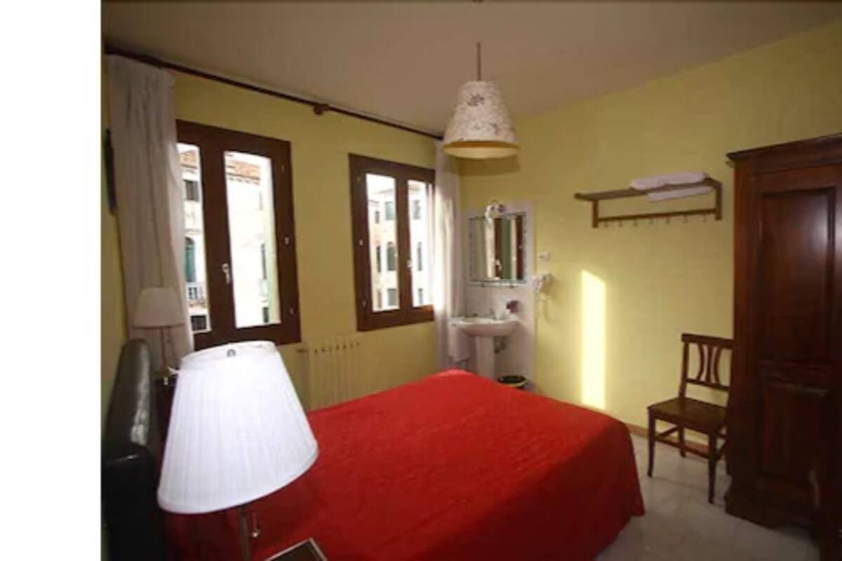 A room with a bed, a chair, a desk, a lamp, a window, and a door.