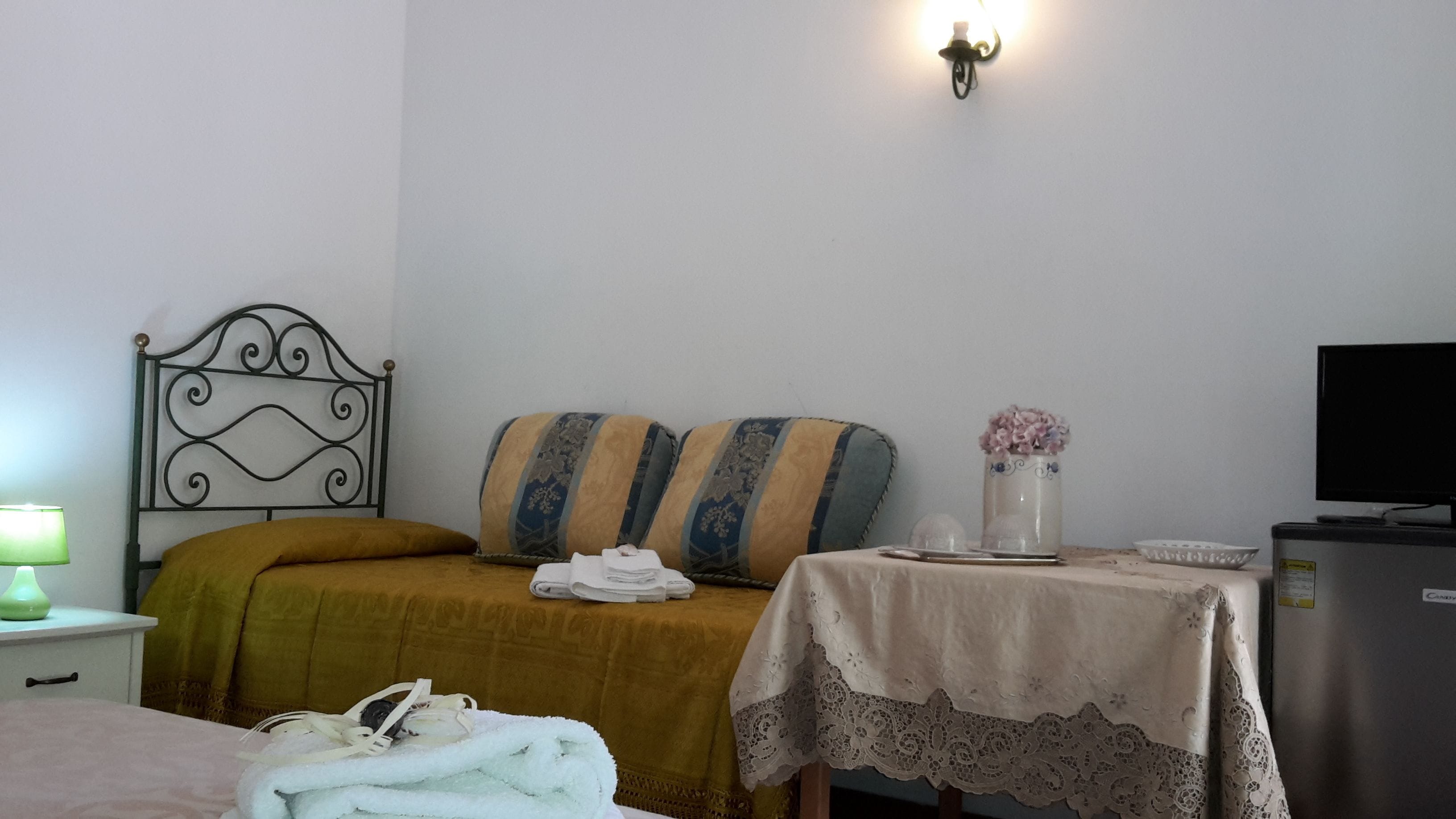 A bedroom with a bed, a nightstand, a table with a vase, and a television.