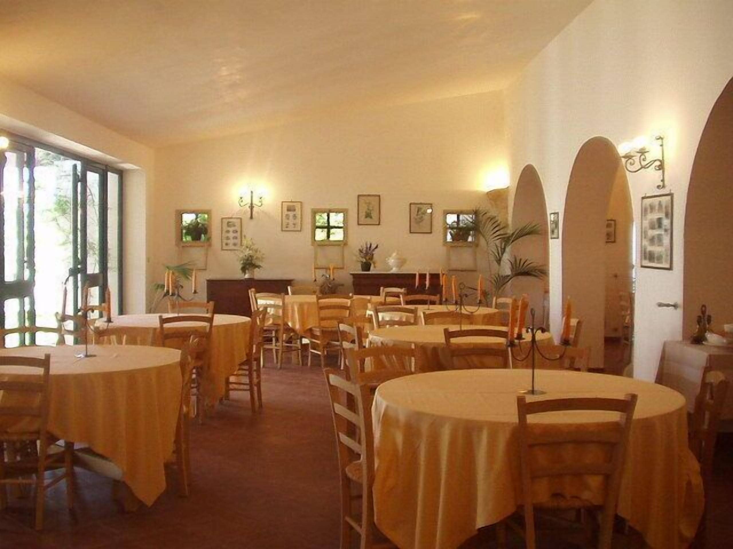 Un comedor con mesas y sillas redondas, cuadros en las paredes y un amplio ventanal que proporciona luz natural.
