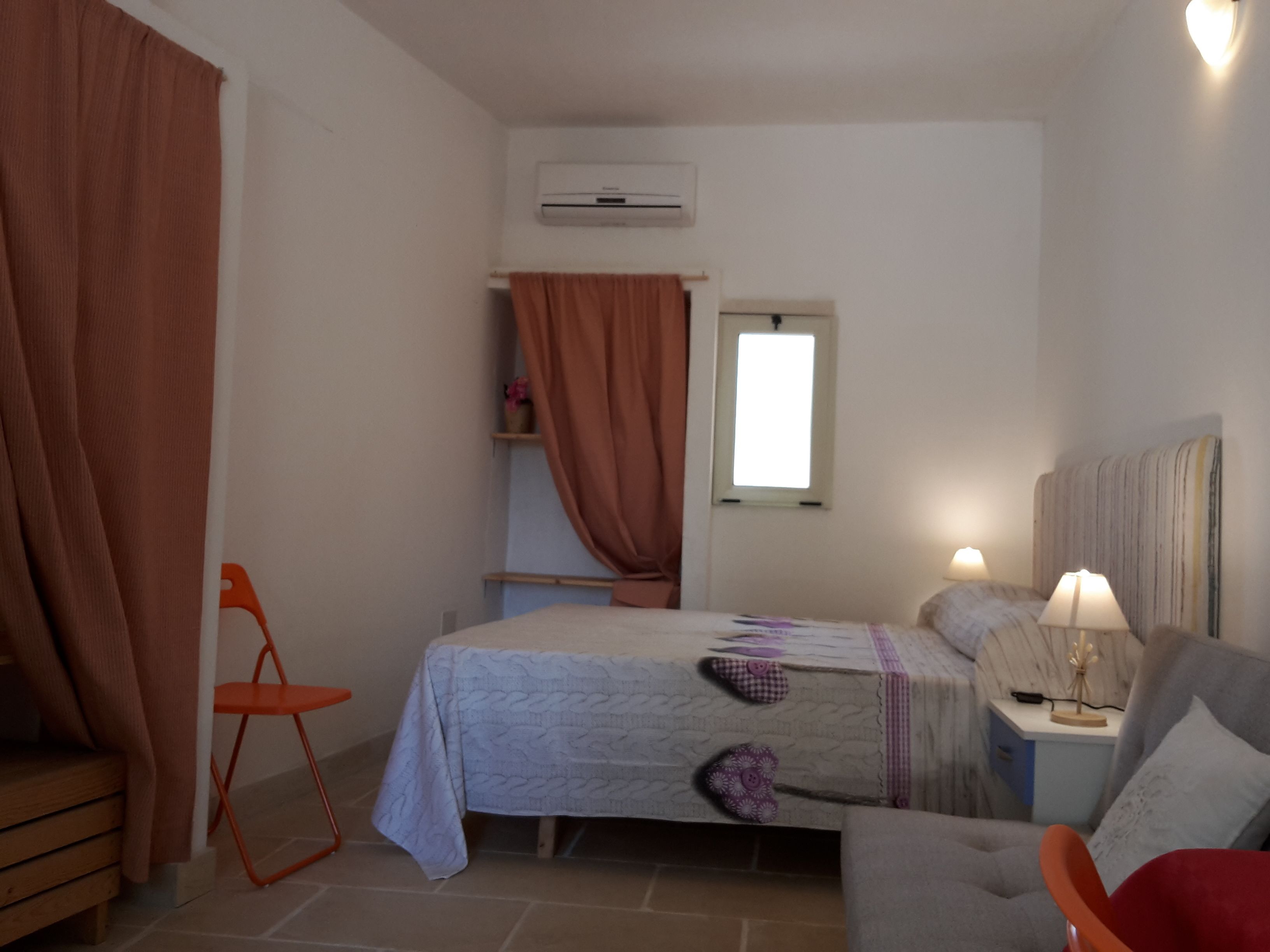 Un dormitorio con cama, mesita de noche, silla, aire acondicionado y ventana.
