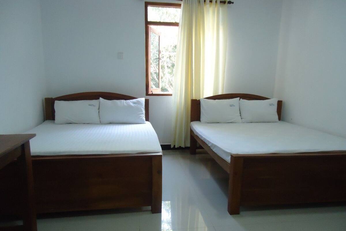 Two wooden beds with white linens in a room with a window and curtains.