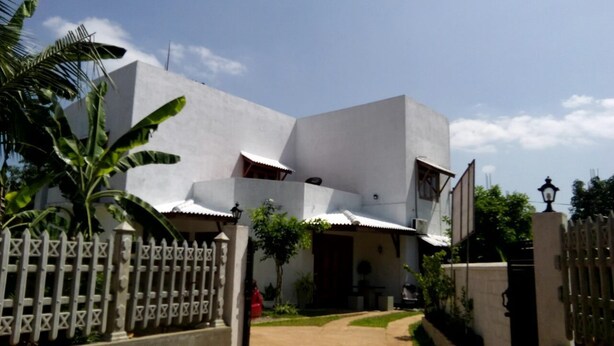 A modern building with a white facade, a gated entrance, and a pathway leading to the main entrance. - Tree House Holiday Home (Anuradhapura)
