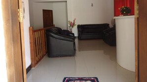 A living room with two black leather sofas, a wooden railing, a white pillar, and a red curtain. - Tree House Holiday Home (Anuradhapura)