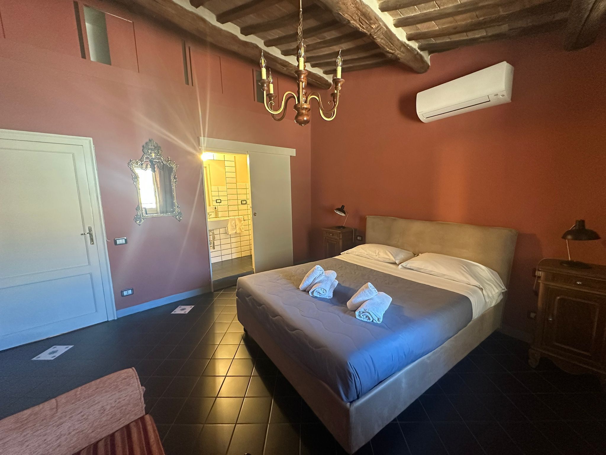 Una camera da letto con un letto, un comodino, una lampada, un armadio, uno specchio e un condizionatore d'aria.