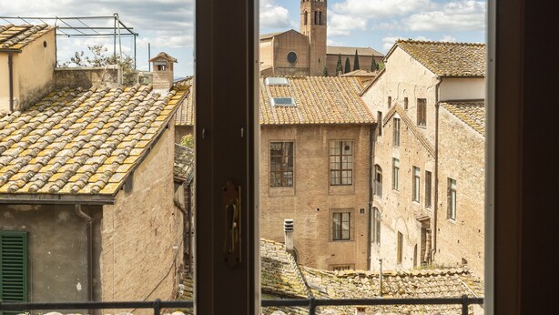 A view of a traditional European town with stone buildings, a church with a bell tower, and a tiled roof. - Birbo Bike Hospitality (Siena)