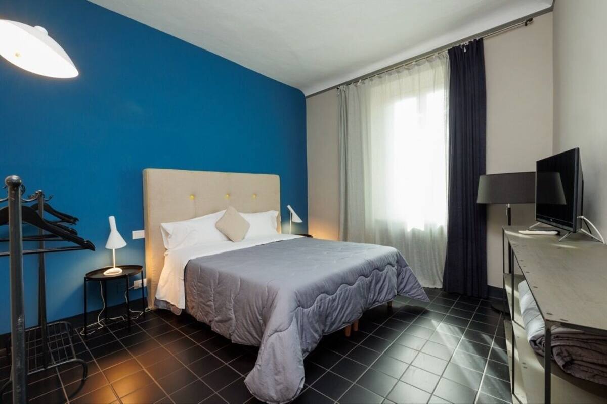 A hotel room with a bed, a desk, a television, a lamp, and a window with curtains.