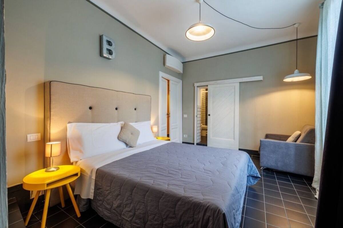 A hotel room with a bed, bedside table, lamp, and a chair.