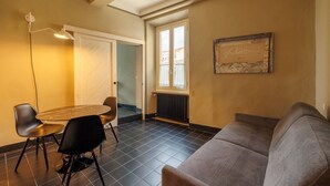 A room with a sofa, a dining table with chairs, a pendant light, a window, and a radiator. - Birbo Bike Hospitality (Siena)