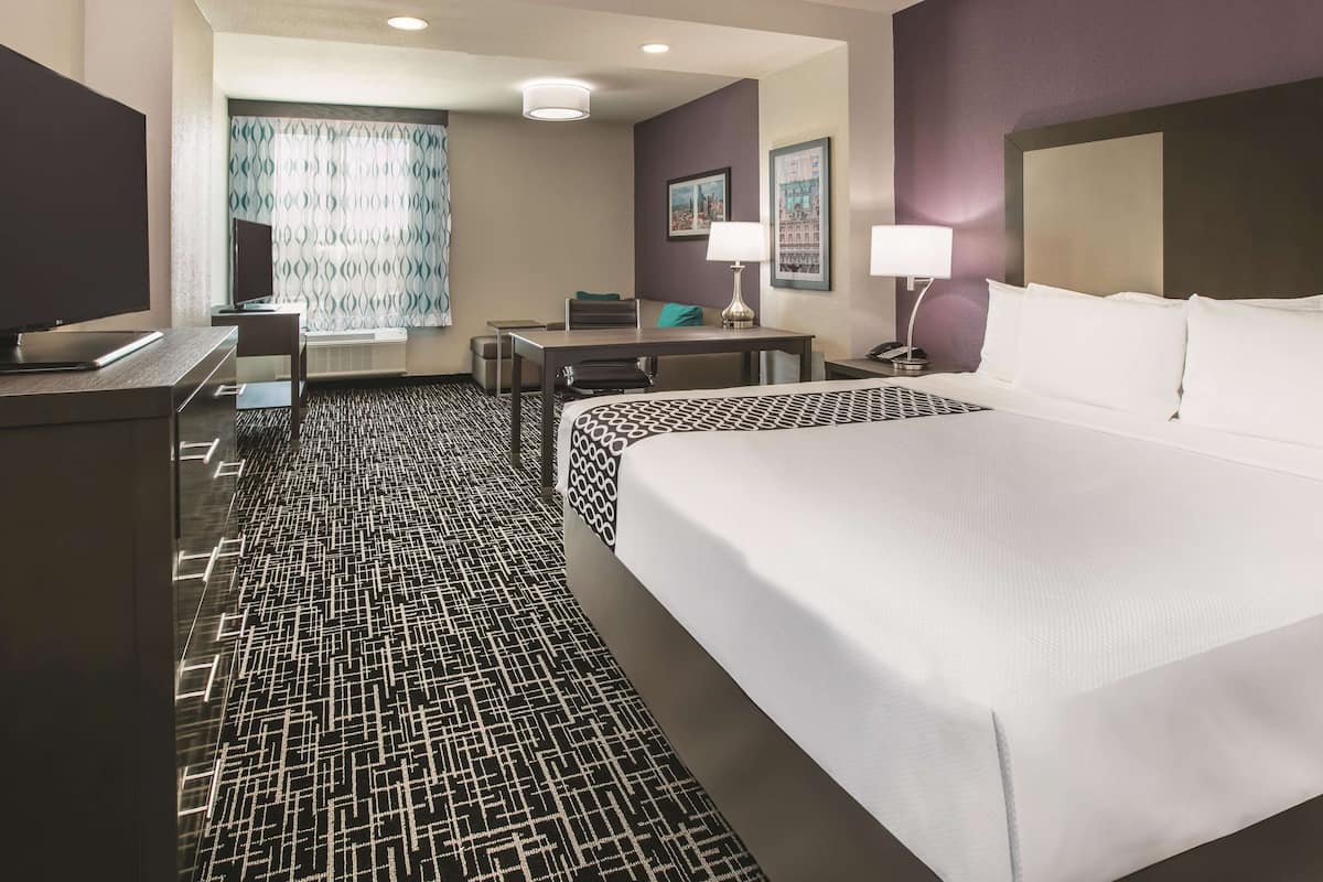 A hotel room with a large bed, a desk, a television, and a patterned carpet.