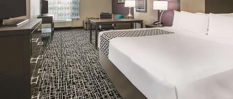 Habitación de hotel con una cama grande, un escritorio, televisión y una alfombra estampada.