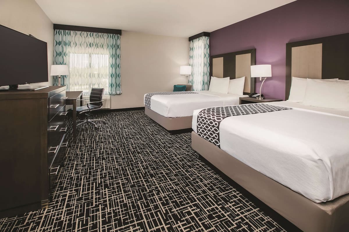 A hotel room with two beds, a desk, a TV, and a patterned carpet.