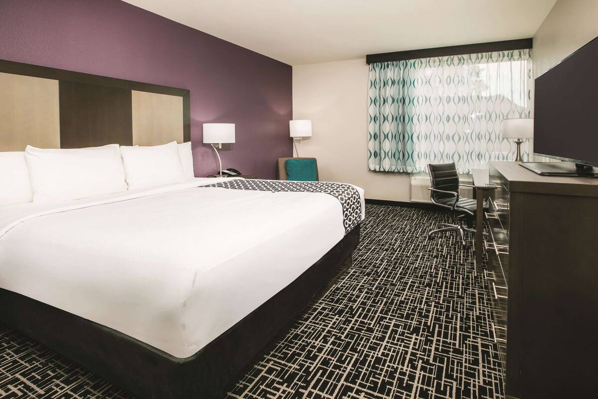 A hotel room with a large bed, a desk, a chair, and a television.
