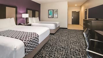 Una habitación de hotel con dos camas, un escritorio con lámpara, televisión y cómoda.
