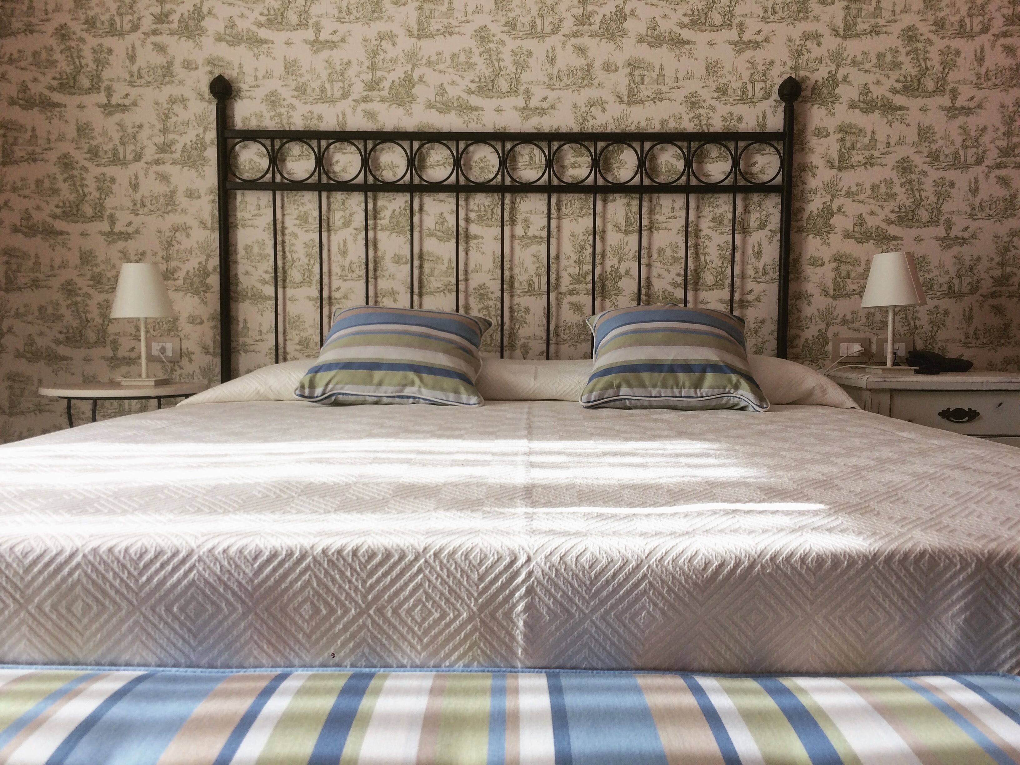 Un letto con una testiera decorata, due cuscini e un comodino con una lampada.