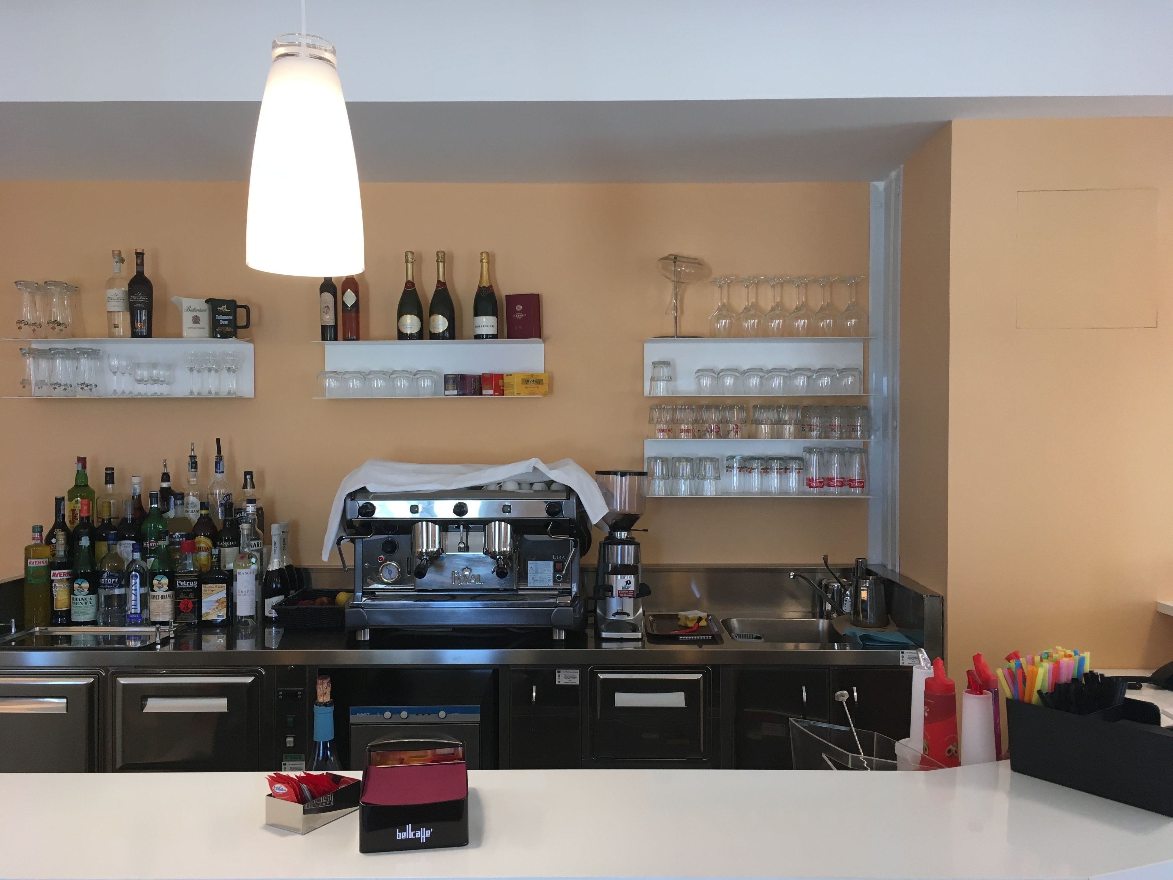 Un espace bar avec des étagères remplies de bouteilles d’alcool, de verres et un appareil à café.