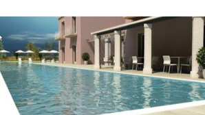 Una piscina con sillas de descanso y sombrillas, un edificio con balcones y un cielo despejado.