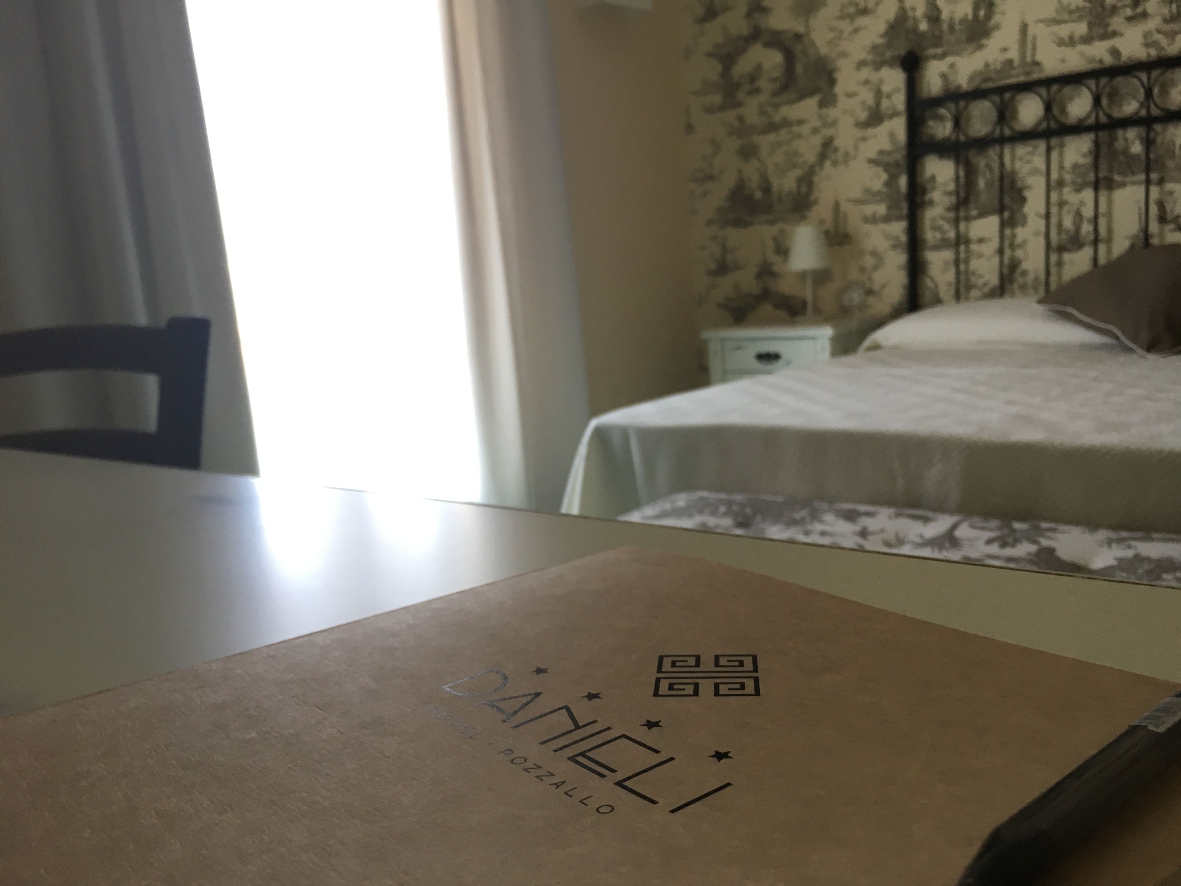 A hotel room with a bed, a nightstand, and a table with a brown box.