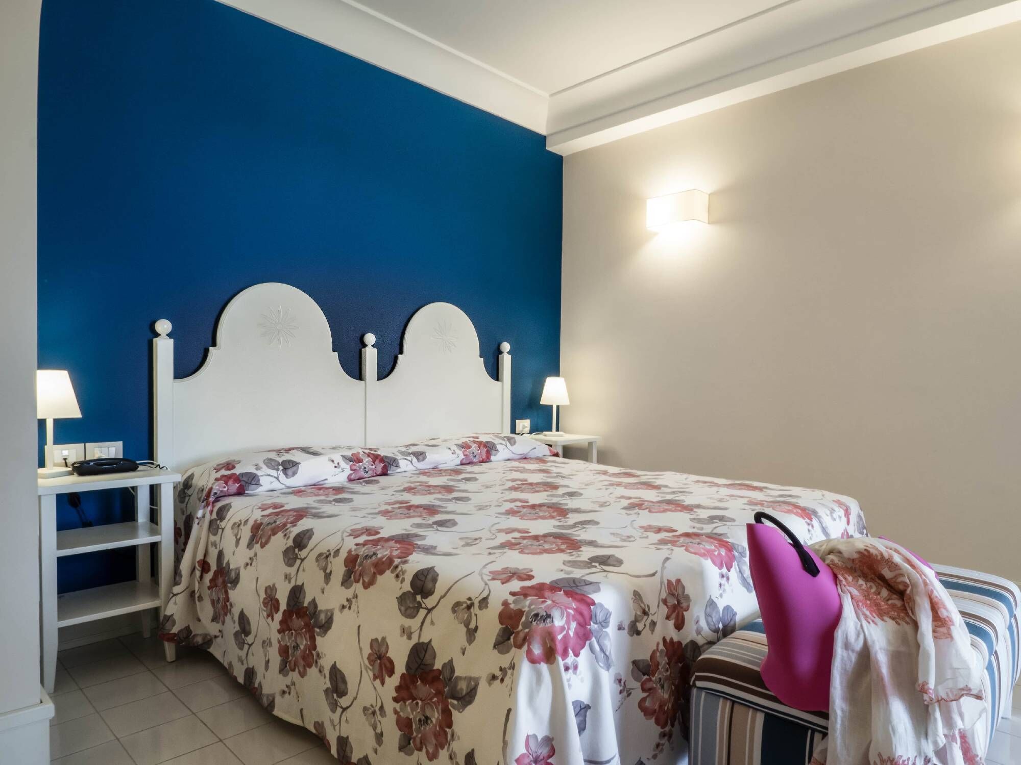 A bedroom with a bed, two bedside tables, a nightstand, and a wall-mounted light fixture.