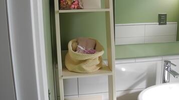 Un bagno con un lavandino bianco, pareti verdi e uno scaffale bianco con un cesto e una borsa.